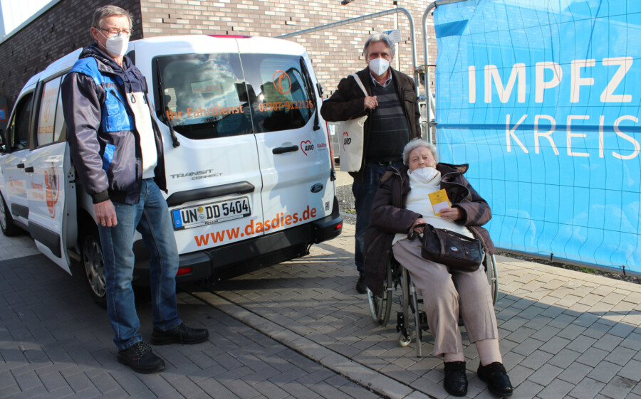 Fahrer Karl-Heinz Hug mit Klaus und Margret Bekemeier (von li.)  nach ihrem Impftermin mit einem „himmlischen Gefühl“ vor dem himmelblauen Transparent des Impfzentrums Unna (Foto: AWO RLE - Stefan Kuster)